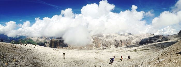 Panoramic view of tourists on landscape against cloudy sky