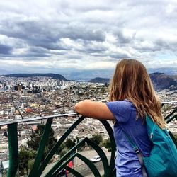 Woman looking at cityscape against cloudy sky