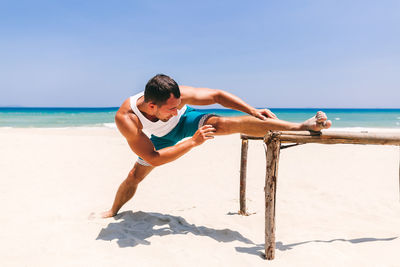 Full length of man exercising at beach against clear sky