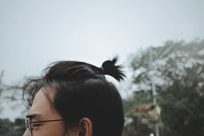 Close-up of young woman with ponytail against sky