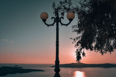 Silhouette street light by sea against sky during sunset