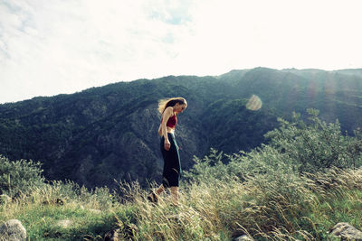 Side view of woman walking on grassy mountain against cloudy sky