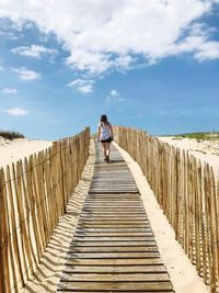 Rear view of woman walking amidst railings at beach against sky