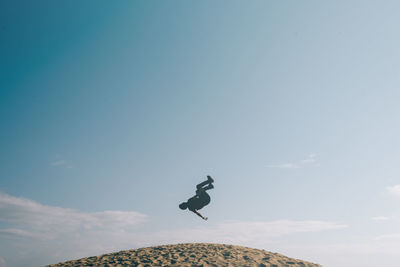 Low angle view of man jumping on hill against sky