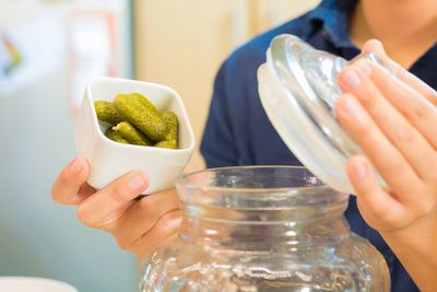 Midsection of person putting pickled cucumbers in jar