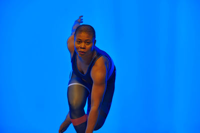 Portrait of young woman standing against blue background