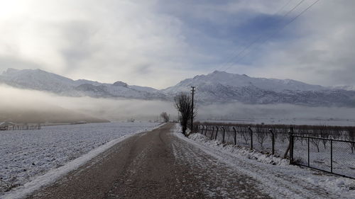 Road leading towards snowcapped mountains against sky