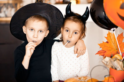 Funny child girl and boy in witch and evil costumes for halloween eating candies lolly pops