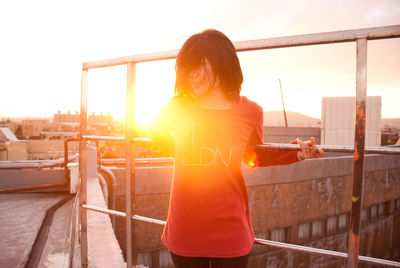 Young woman standing while holding railing on building terrace at morning