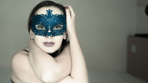 Portrait of young woman wearing venetian mask at home