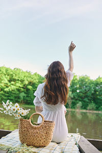 Rear view of woman sitting on retaining wall against sky