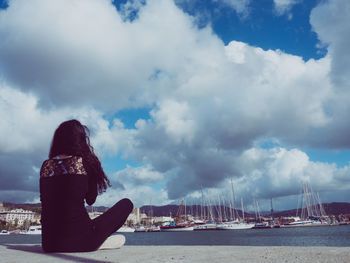 Rear view of woman sitting by sea against sky