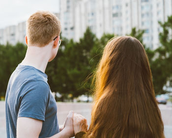 Rear view of couple holding hands against buildings in city