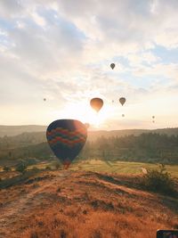 Hot air balloons flying over landscape against cloudy sky