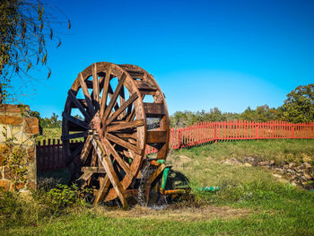 Wooden water wheel on field against clear blue sky