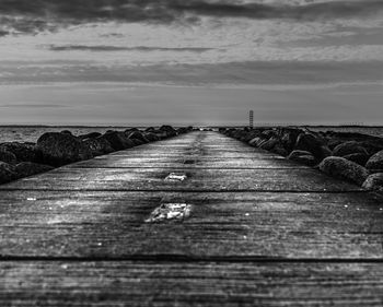 Surface level of wooden walkway by sea against sky