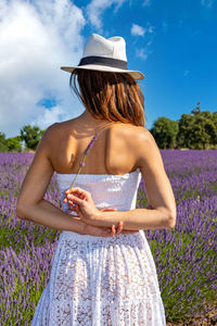 Back view of a woman in a blooming field with a spring of lavender in her hands. 