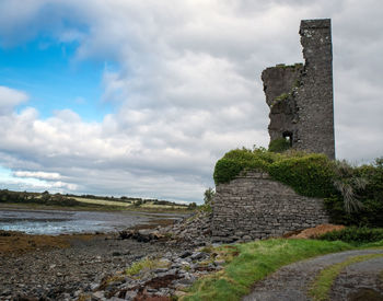 Old ruin building at beach against cloudy sky