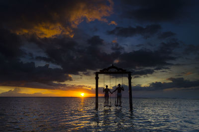 Silhouette people by sea against sky during sunset