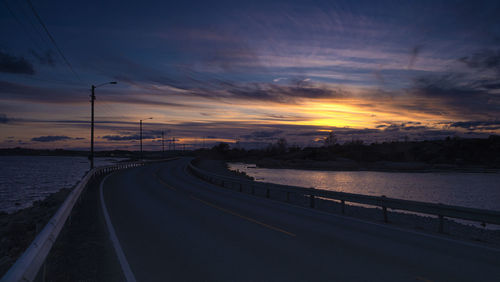 Road by river against sky at sunset