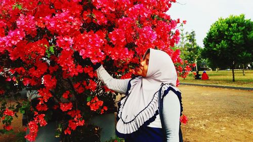 Rear view of woman standing by red flowering plants