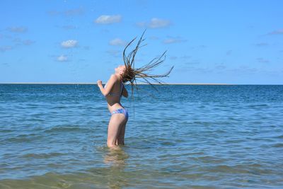 Girl tossing hair in sea against sky