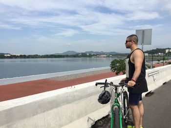 Cyclist with bicycle on street looking at lake against sky