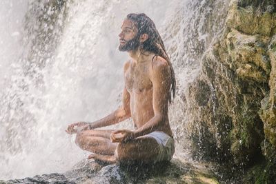 Full length of shirtless man sitting in water