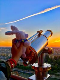 Close-up of hand holding camera against sky during sunset