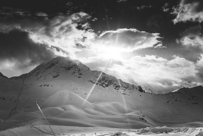 Black and white of the sun shining through the clouds above a ski slope in les arcs