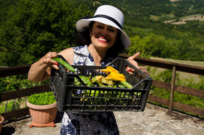 Portrait of smiling woman carrying vegetables in container