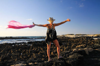 Rear view full length of woman with arms outstretched standing on rocks at beach