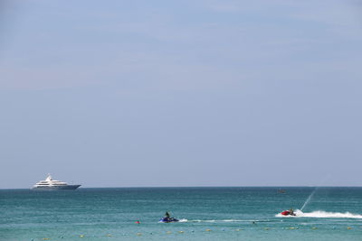 People riding motorboats on sea against clear blue sky