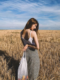 Young woman standing on field against sky