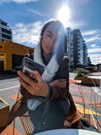 Portrait of young woman using smart phone while sitting at sidewalk cafe