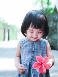 Cute girl holding flower while standing on footpath