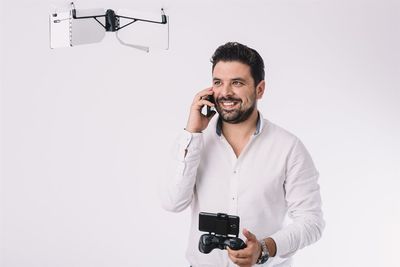 Man talking on phone while flying drone against white background