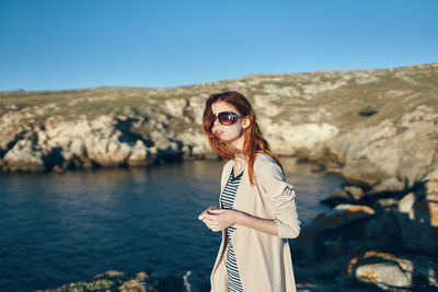 Portrait of young woman wearing sunglasses standing against clear sky