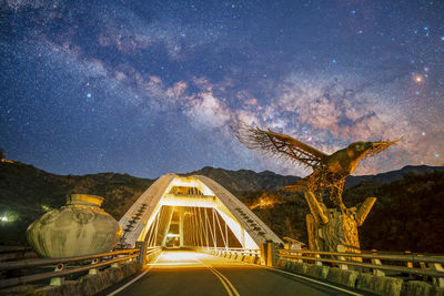 Road by illuminated bridge against sky at night