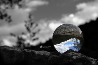 Close-up of crystal ball on rock against sky