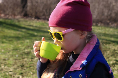 Smiling child in colorful clothes drinking tea from green reusable cup. eco-friendly family picnic.