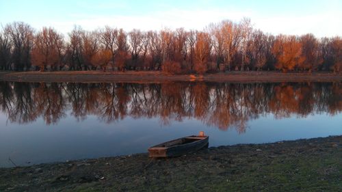 Boat moored on lake by trees against sky