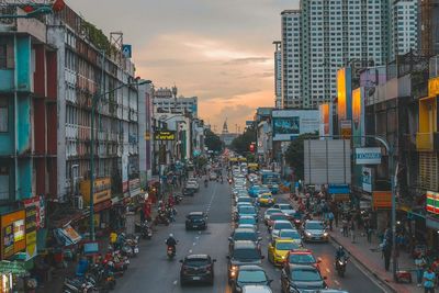 Traffic on city street by buildings against sky during sunset