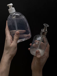 Midsection of woman holding glass bottle against black background
