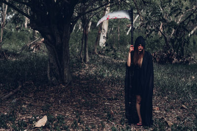 Woman standing by tree trunk in forest