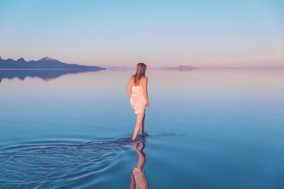 Rear view of woman walking in lake at bonneville salt flats against clear sky