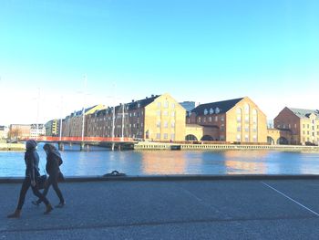 Women walking on promenade by canal against clear sky