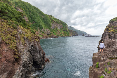 Scenic view of sea by mountain against sky