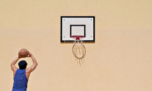 Rear view of man playing basketball against wall