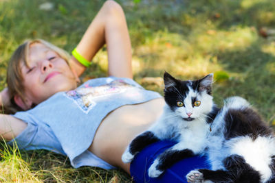 Blonde little girl lying on grass with cat, black and white small cute kitten with yellow eyes.